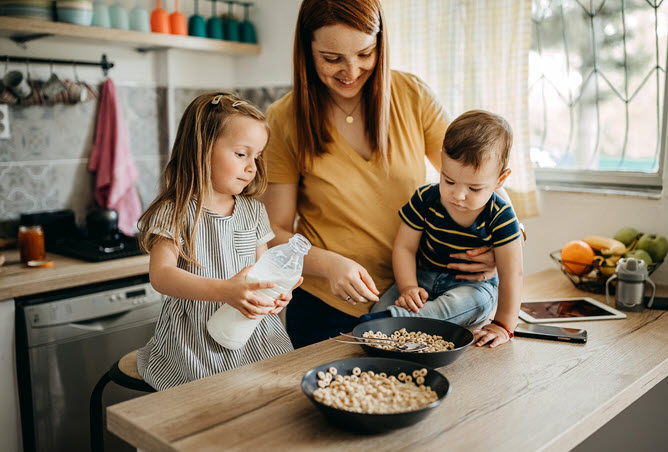 Young Daughter Pouring Milk On Cereal