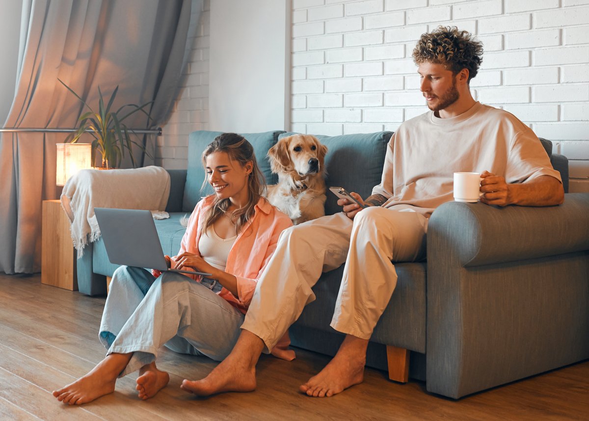 Young Couple In Living Room On Laptop and Phone